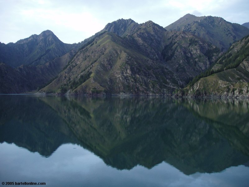 Mountains and clouds reflected in the calm evening waters of Tianchi Lake in Xinjiang province, China