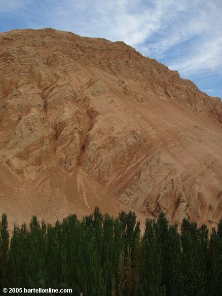 A red-tinted mountain rises above the trees near Bezeklik Grottos in Xinjiang province, China