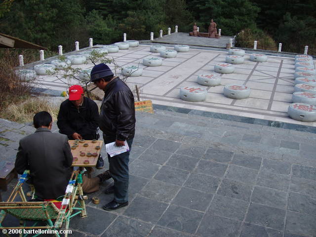 Men play Chinese chess in front of a much larger board near the end of "Cloudy Tourist Road" above Dali, China