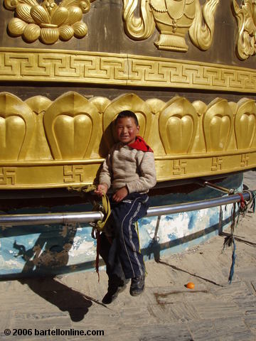 Small boy rides the giant Buddhist prayer wheel in Zhongdian ("Shangri-La"), Yunnan, China
